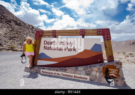 AUGUST 4 2018 - DEATH VALLEY, CALIFORNIA: Sign for Death Valley National Park on an overcast summer day.. Woman photographer poses next to sign Stock Photo