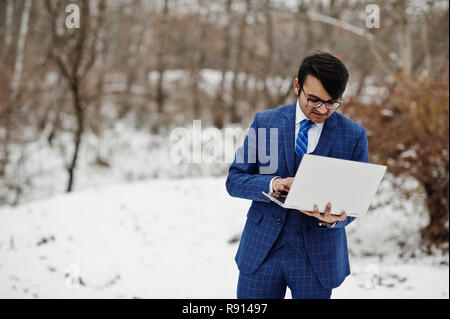 Stylish indian business man in suit and glasses posed at winter day outdoor with laptop at hands. Stock Photo