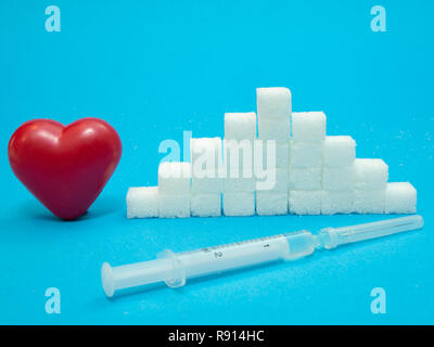 red heart, pile of white refined sugar cubes and syringe with insulin on blue background, diabetes concept Stock Photo