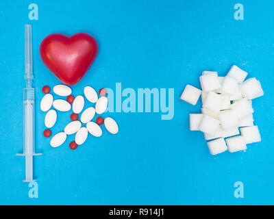 high level of sugar in blood cause heart disease. pills, drugs, red heart and syringe of injection and white blocks of refined sugar on blue backgroun Stock Photo