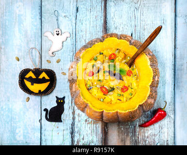 Soup with lentil in the carved pumpkin, Halloween toys on the blue wooden background Stock Photo