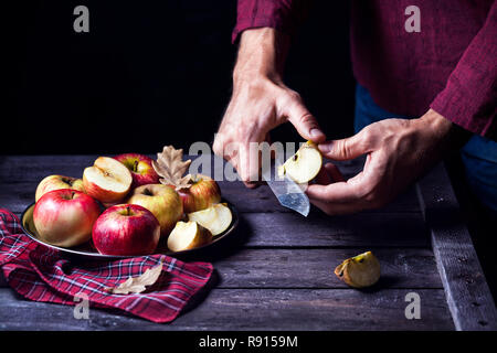 Man cutting red apples on wooden table at dark background. Free space for text Stock Photo