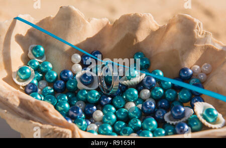 Pair of white gold wedding bands rings hung on blue ribbon in seashell romantic tropical beach ceremony Stock Photo