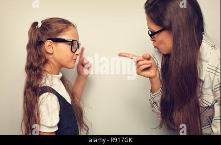 Angry beautiful woman in eye glasses scolding her pupil daughter and shwoung the finger on toned color background Stock Photo