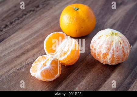 Three satsuma oranges on a rustic wood table, two oranges peeled, one sectioned Stock Photo