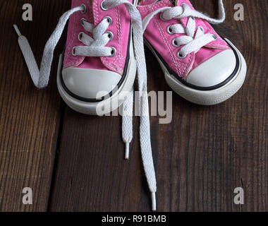 small pink textile sneakers on a brown wooden background, top view Stock Photo