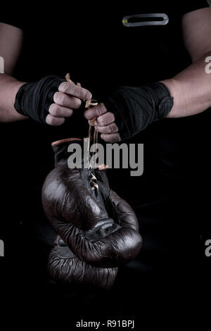 pair of very old boxing sports gloves in men's hands rewound with a black bandage Stock Photo