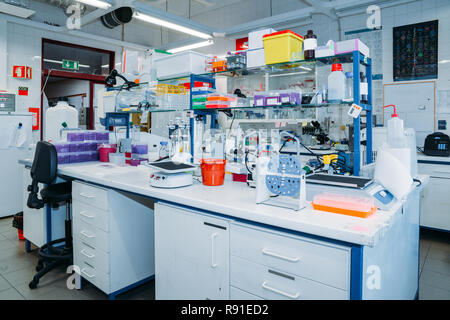 Interior of modern laboratory: desk with Petri dishes, test tubes, flasks and modern microscope on foreground Stock Photo