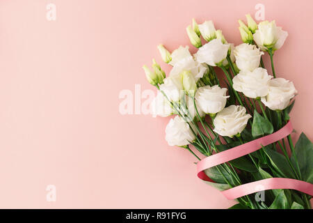 From above bunch of white roses with pink ribbon placed on pink background. Stock Photo