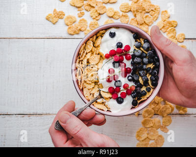 Bowl with healthy breakfast in the hands, cornflakes, yogurt and fresh berries on the background of a whiteboard. Closeup, top view, isolated. Concept Stock Photo