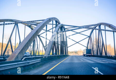 Big rig long haul semi truck transporting covered semi trailer with co commercial cargo driving on the winter frosty arched truss bridge with connecte Stock Photo