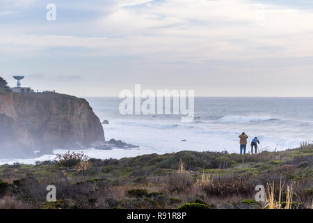 Dramatic landscape of the Pacific Ocean coast, Pillar Point, Half Moon Bay, California; huge waves and surfers visible in the background; tourists wat Stock Photo