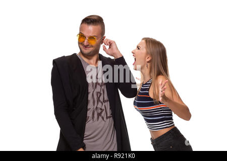 Angry blonde young European woman gestures with hands, shouts at husband who is guilty, stands together against white background, have dispute and quarrel Stock Photo