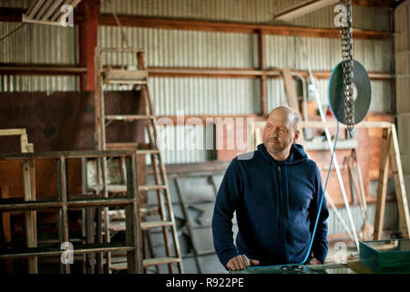 Mid adult man looking thoughtful while standing in a workshop. Stock Photo