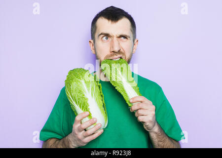 Young man biting on a leaf of Beijing napa cabbage, doubt face expression. Light purple background. Stock Photo