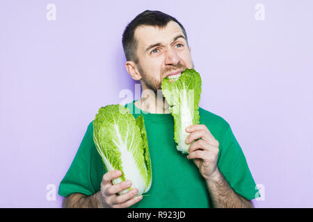 Young man biting on a leaf of Beijing napa cabbage, doubt face expression. Light purple background. Stock Photo