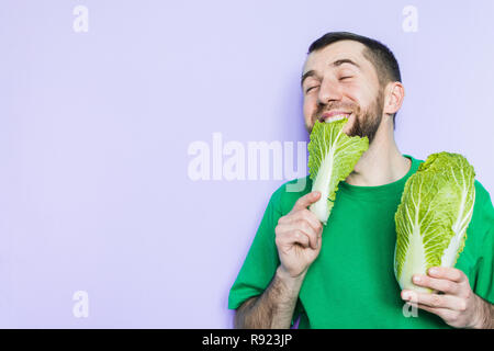 Young man biting on a leaf of Beijing napa cabbage, enjoyment face expression. Light purple background, copy space. Stock Photo