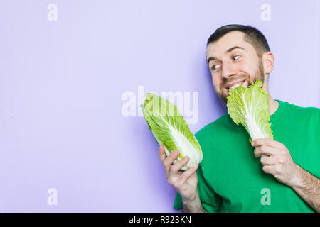 Young man biting on a leaf of Beijing napa cabbage, enjoyment face expression. Light purple background, copy space. Stock Photo