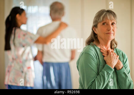Senior woman looking hopeful while a nurse comforts her unwell husband. Stock Photo