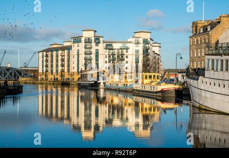 Leith, Edinburgh, Scotland, United Kingdom. 19th Dec, 2018. UK Weather: a beautiful sunny Winter day in the capital city with the lack of wind creating reflections in the Water of Leith river. Queen's Quay, a modern apartment development is reflected in the water as well as several river barges or houseboats Stock Photo