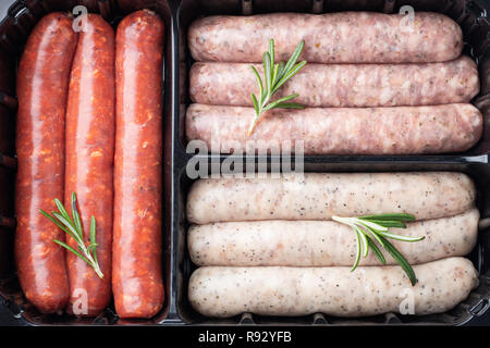 Plastic tray with fresh raw pork and beef sausages with rosemary. Top view. Stock Photo