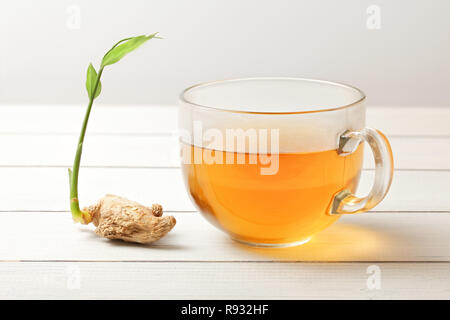 Cup of ginger tea (hot steam and moisture drops on glass), dry root with green spring next to it. Stock Photo