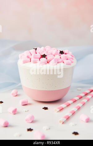 Hot chocolate or cocoa with whipped cream and pink marshmallow candy decorated with sugar snowflakes and chocolate stars in pink and white mug on whit Stock Photo