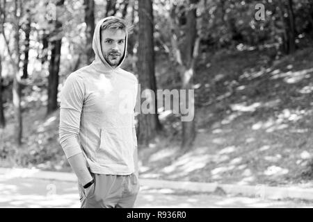 Taking minute break. Runner workout outdoor. Man athlete with hood after running outdoor, nature background. Athletic man relaxing break. Athlete hooded takes break during exhausting training. Stock Photo