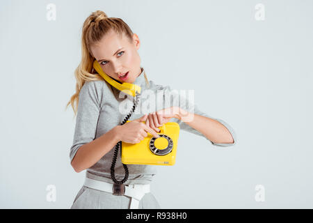 beautiful woman dialing phone number on vintage yellow telephone isolated on grey Stock Photo