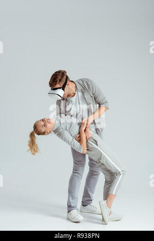 man holding woman in embrace while having virtual reality experience on grey background Stock Photo