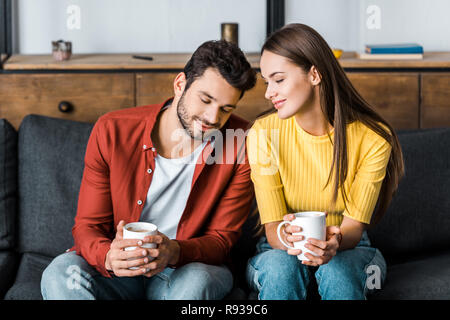 happy couple sitting on sofa and holding cups with drinks Stock Photo