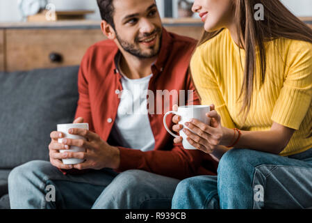 cropped view of happy couple sitting with cups in living room Stock Photo