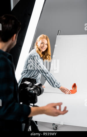 cropped shot of male photographer looking at colleague arranging shoe in studio Stock Photo