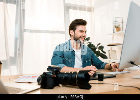 smiling young photographer using desktop computer and retouching photos at workplace Stock Photo