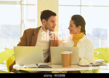 loving couple sitting at table with laptops and looking at each other in cafe Stock Photo