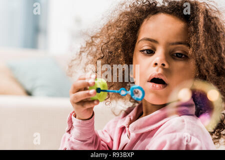 curly african american kid blowing soap bubbles at home Stock Photo