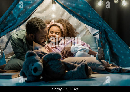 african american dad and daughter lying in wigwam Stock Photo
