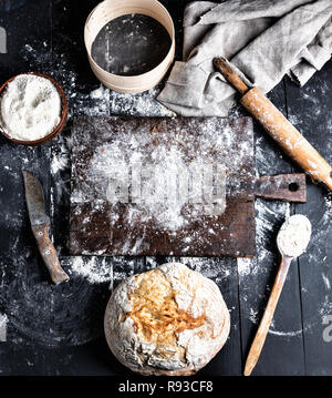 baked bread, white wheat flour, wooden rolling pin and old cutting board on a black table, top view Stock Photo