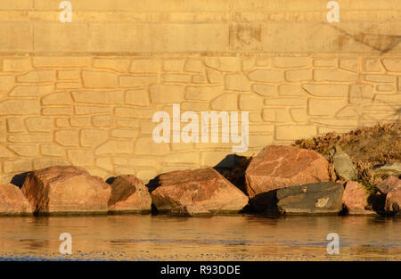 Wall with rocks on edge of lake with golden hue at sunset Stock Photo