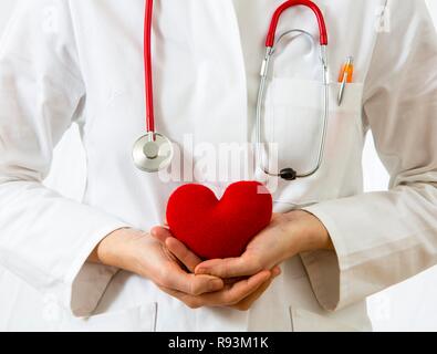 Female doctor holding a red heart in her hands, symbolic image for a heart attack Stock Photo