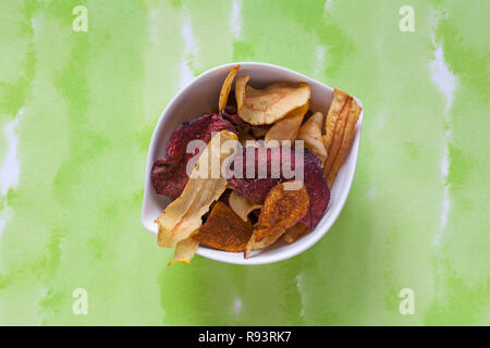 Bowl of Tyrrells veg crisps hand-cooked English crisps isolated on green patterned background - parsnip, beetroot & carrot crisps with sea salt Stock Photo