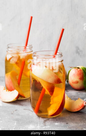 Peach nectarine cold ice tea lemonad different ingredients two glasses jar on gray background. Stock Photo