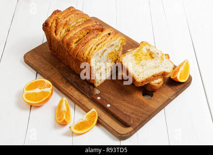 Homemade bread with orange zest and walnuts on white wooden table. Near a knife and slices of fresh oranges. Stock Photo