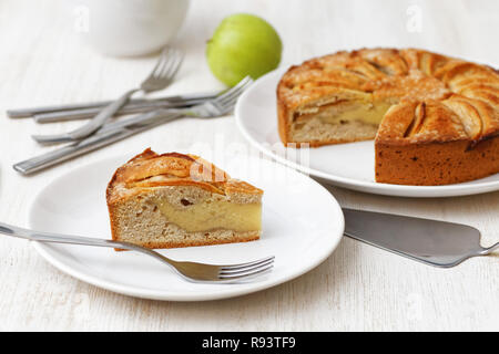 Homemade apple custard pie topped with slices of apples and cinnamon on white wooden table. Shallow focus. Stock Photo