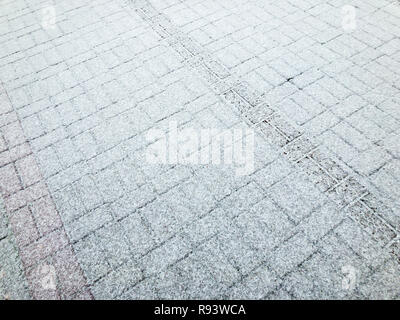 snow covered paving tiles after snowfall. winter background with tire track imprint Stock Photo