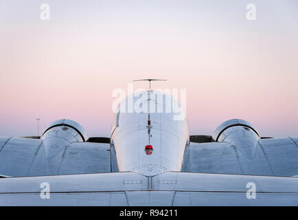 Symmetrical rear view of vintage chrome twin prop passenger airplane against a pink dusk sky Stock Photo