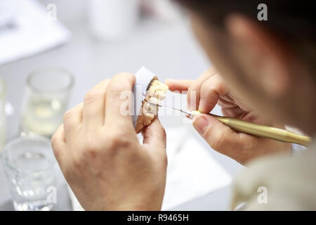 Dental technician working on a dental casting. Hand of dental technician working with acrylic for tooth modeling Stock Photo
