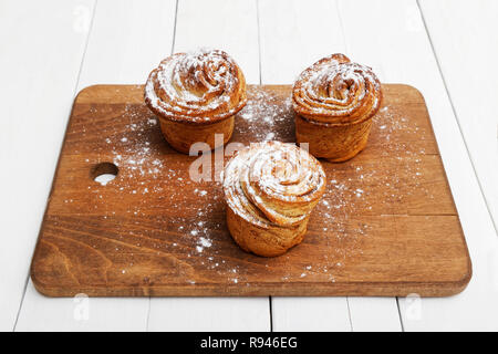 Three homemade cinnamon rolls from yeast dough sprinkled with powdered sugar on wooden cutting board Stock Photo