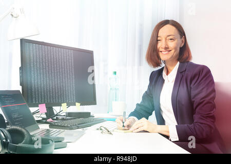 Portrait of businesswoman making notes with a pen, sitting at the desk in the office, smiling and looking camera Stock Photo
