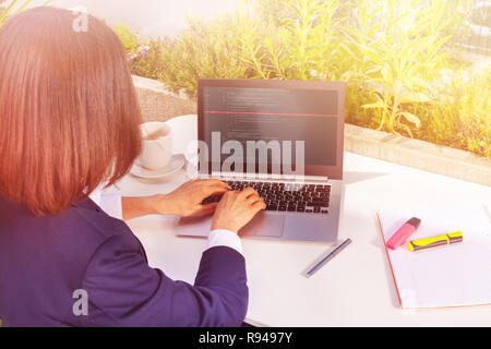 Rear view of businesswoman working with laptop, sitting at a table of street cafe Stock Photo